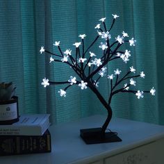 a small tree with white flowers sitting on top of a table next to a book