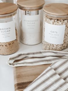 three jars with labels on them sitting next to a dish towel and wooden cutting board