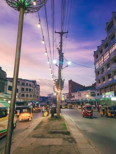 the city street is crowded with cars and buses at dusk, while people are walking on the sidewalk