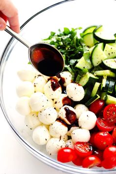 a bowl filled with tomatoes, cucumbers, and other veggies being drizzled with sauce