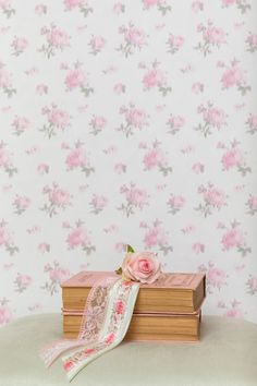 a stack of books sitting on top of a table next to a flower covered wall