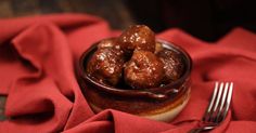 a small bowl filled with meatballs on top of a red cloth next to a fork