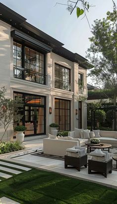 an outdoor living area with white furniture and green grass in front of a large house