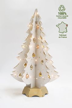 a white christmas tree with gold ornaments on it's base and lights in the shape of trees