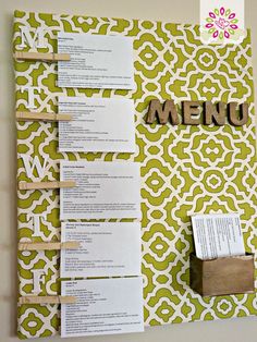 a green and white wall hanging with some paper on it, next to a wooden block that says menu