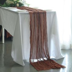 a table with a white cloth and some brown yarn on it, in front of a window