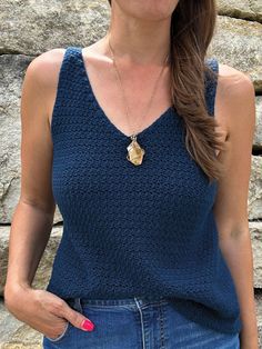 a woman standing in front of a rock wall wearing a blue tank top and jeans