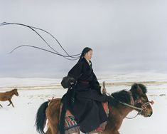 a woman riding on the back of a brown and black horse in snow covered field