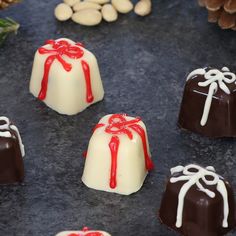 chocolates with white and red toppings are arranged on a black surface next to pine cones