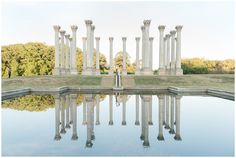 a man standing in front of a body of water surrounded by tall white pillars and columns