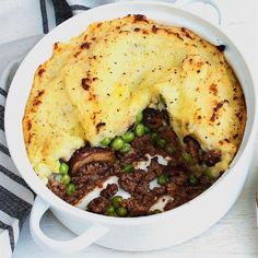 a casserole dish with meat, potatoes and peas in it on a table