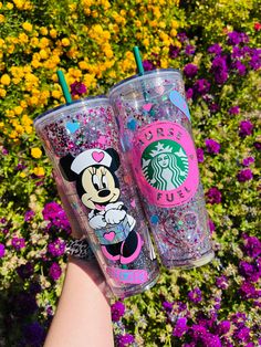 two starbucks cups with minnie mouse designs on them are held in front of some flowers