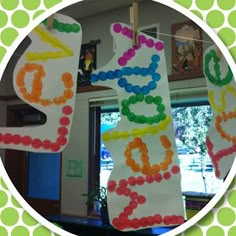 a circle frame with colorful paper letters hanging from it's sides in front of a green and white polka dot wall