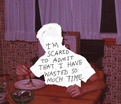 a person sitting at a table with a sign on it that says i'm scared to admit that i have wasted so much time