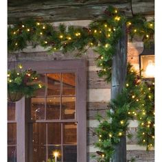 christmas lights are hanging on the side of a log cabin building with wreaths and potted plants