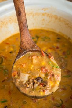 a wooden spoon filled with soup and vegetables