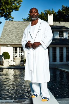 a man standing in front of a swimming pool wearing white clothing and yellow shoes with his hands on his hips