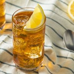 two glasses filled with ice and lemon on top of a striped table cloth next to spoons