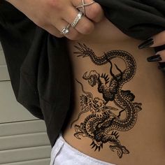 a woman's stomach with a dragon tattoo on the side and her hand holding it