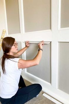 a woman sitting on the floor in front of a wall with white paneling and paint