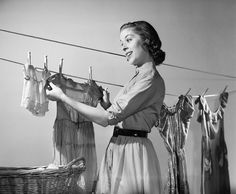 an old photo of a woman hanging clothes on a line