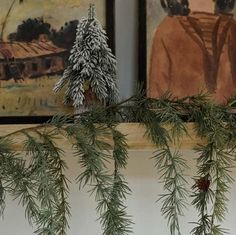 pine needles hang from the top of a mantle in front of two paintings on display