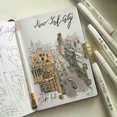 an open notebook with drawings on it and some pencils next to it, along with two pens