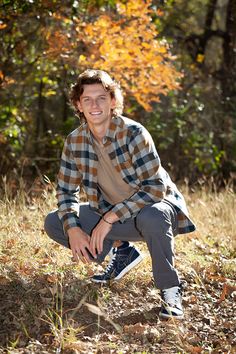 a young man sitting on the ground in front of trees