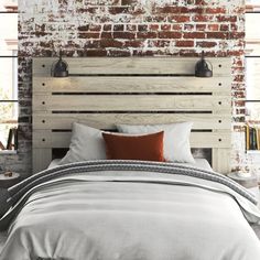 a bed with white linens and pillows in front of a brick wall behind it