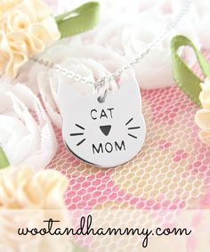 a cat mom necklace with a heart on it and flowers in the background, sitting on top of a bed of fabric