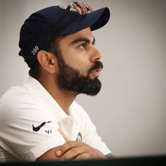 a man with a beard wearing a baseball cap and looking off to the side while sitting in front of a computer