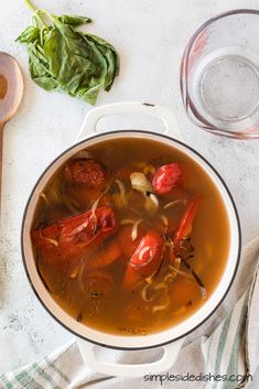 a pot filled with soup next to a wooden spoon and some spinach on the side