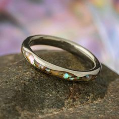 This magnificent abalone wedding band has a presence like no other. The vibrant glow of crushed abalone gives this 14k yellow, rose or white gold ring a dazzling display. A wavy design is fashioned in the gold edges, adding to the whimsical nature of this sea shell ring.RING LAYOUT Ring Width: 3 mm Ring Sleeve: 14k Gold Ring Profile: Wavy Ring Finish: Polished0.5 mm 14k Gold 2 mm Crushed Abalone 0.5 mm 14k GoldThis ring is made with a comfort fit.RING FITTING:We highly recommend that you get you Tension Set Engagement Rings, Wavy Ring, Abalone Ring, Whimsical Nature, Wavy Design, Wedding Band Designs, Wavy Style, Shell Ring, Solid Gold Rings