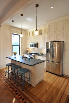 a kitchen with an island and three stools in front of the sink, refrigerator and microwave