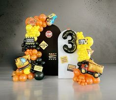 an assortment of balloons and decorations are arranged in the shape of cars, trucks, and numbers