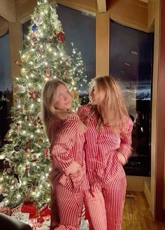 two women in pajamas standing next to a christmas tree