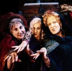 three women dressed as witches posing for the camera with their hands in the air and smiling