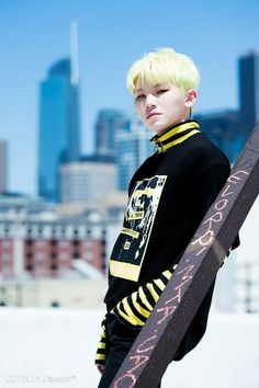 a young boy with blonde hair is holding a skateboard in front of a cityscape