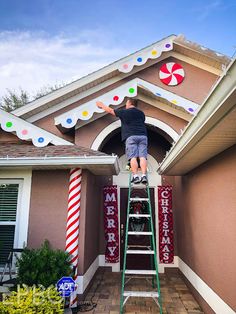 a man on a ladder painting the roof of a house with christmas decorations and candy canes