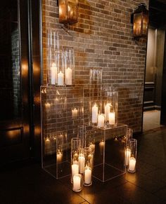 candles are lit in clear glass containers on the floor next to a brick wall with hanging lights