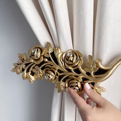 a hand is holding a curtain with gold flowers on it