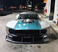 a blue and white muscle car parked in front of a gas station at night time