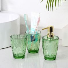 three green glass cups with toothbrushes and soap dispenser sitting on a counter