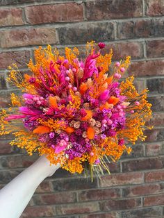 a hand holding a bouquet of flowers in front of a brick wall with orange and pink colors