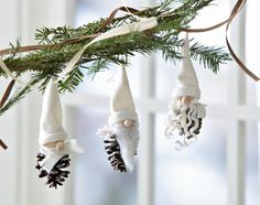 three ornaments hanging from a tree branch with pine cones on them and white knitted hats