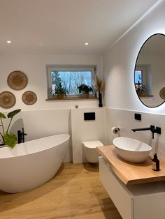 a bathroom with a large white bathtub next to a wooden counter top under a round mirror