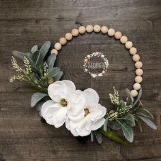 white flowers and greenery are arranged on a wooden table with a personalized bracelet