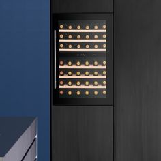 a wine cooler with several bottles in front of it and a blue wall behind it