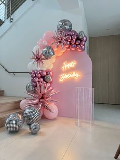 a pink and silver balloon arch with happy birthday written on it in front of stairs