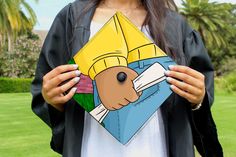 a woman holding an origami piece in front of her face and wearing a graduation cap